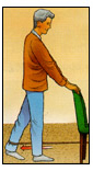 Post operative male patient standing behind and holding onto a chair performing Resistive Hip Extensions