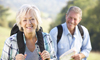 A senior woman and gentleman carrying backpacks and smiling enjoying a nature walk
